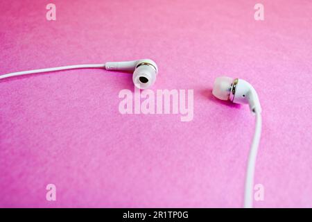 Magnifique casque numérique moderne à dépression en plastique blanc avec fils pour écouter de la musique sur fond rose violet. Copier l'espace. Banque D'Images