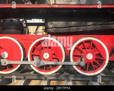Grandes roues en fer d'un train rouge et noir debout sur des rails et des éléments de suspension avec ressorts d'une ancienne locomotive industrielle à vapeur. Banque D'Images
