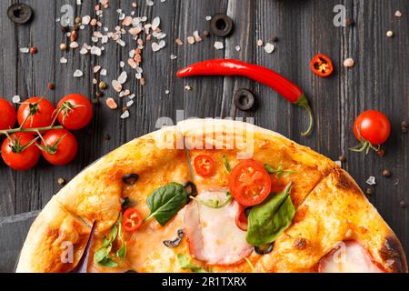 Pizza avec jerky, olives, fromage, herbes et légumes frais sur une assiette en pierre noire sur fond de bois sombre. Cuisine italienne traditionnelle. Banque D'Images