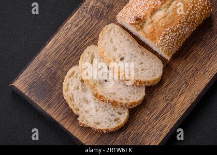 Baguette de farine de blé croustillante aux graines de sésame sur une planche à découper en bois sur fond de béton foncé Banque D'Images