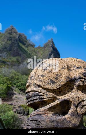 Polynésie française, Marquises méridionales, Fatu Hiva, village d'Omoa. Sculpture traditionnelle en pierre tiki avec des montagnes volcaniques abruptes au loin. Banque D'Images