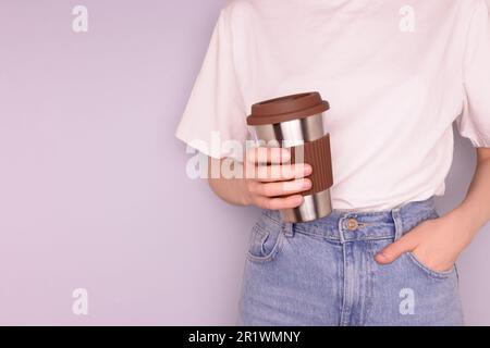 Femme méconnaissable dans un t-shirt blanc tenir dans les mains tasse à café réutilisable devant un fond bleu. Concept de boissons à emporter avec espace de copie. Banque D'Images