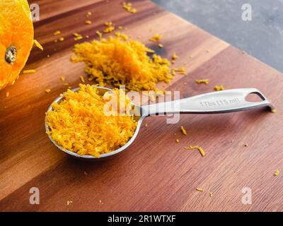 Cuillère à soupe de zeste d'orange frais sur une planche à découper en bois : vue rapprochée à angle bas du zeste d'orange dans une cuillère de mesure Banque D'Images