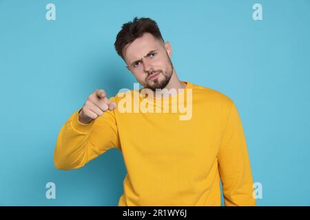 Homme agressif dans un sweat-shirt jaune pointant vers quelque chose sur fond bleu clair Banque D'Images