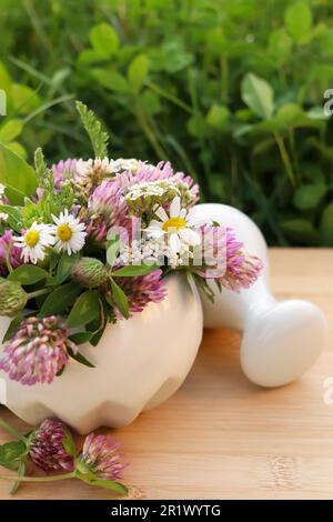 Mortier en céramique avec pilon, différentes fleurs sauvages et herbes sur l'herbe verte à l'extérieur Banque D'Images