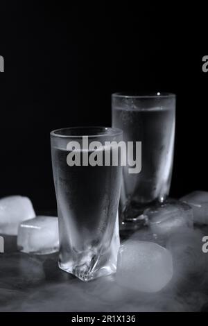 Vodka en verres à liqueur avec glace sur table sur fond noir Banque D'Images