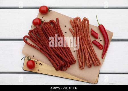 Délicieux kabanosy avec tomates, grains de poivre et piment sur une table en bois blanc, vue du dessus Banque D'Images