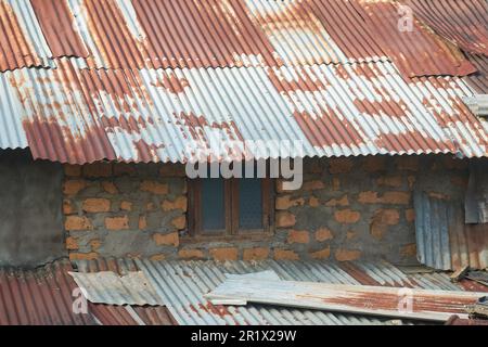 vue rapprochée de l'ancienne maison de bidonville endommagée, bâtiment temporaire fait de mur de brique non cuite avec du ciment et des tôles de couverture ondulée en métal rouillé Banque D'Images