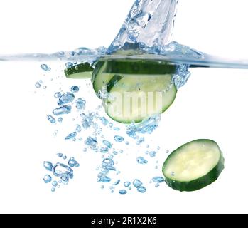 Tranches de concombre frais tombant dans l'eau sur fond blanc, gros plan Banque D'Images
