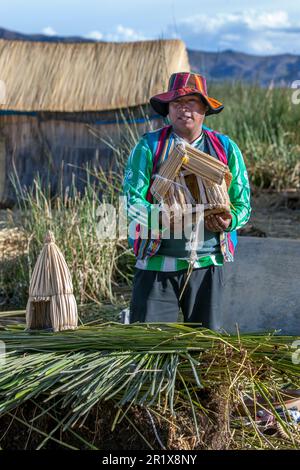 Un homme présente des maisons miniatures en roseau modélisées sur les versions pleine grandeur construites sur les îles flottantes d'Uros sur le lac Titicaca au Pérou. Banque D'Images