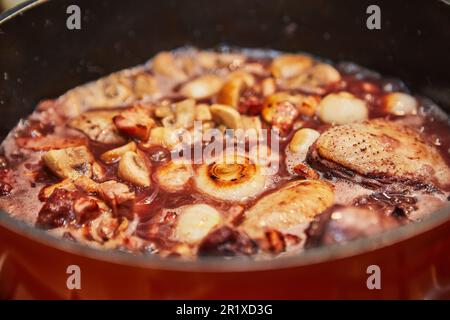 Poulet mariné au vin rouge avec romarin dans une casserole avec oignons et champignons sur cuisinière à gaz Banque D'Images