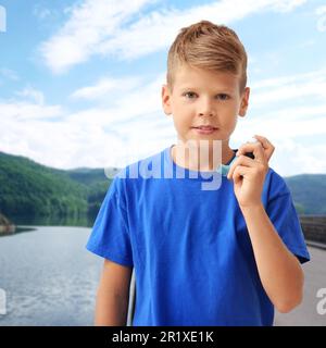 Petit garçon avec un inhalateur d'asthme près du lac. Premiers soins d'urgence pendant les loisirs en plein air Banque D'Images