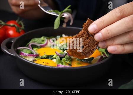 Femme trempant un morceau de pain dans le jaune d'œuf, gros plan. Manger un Shakshuka savoureux Banque D'Images