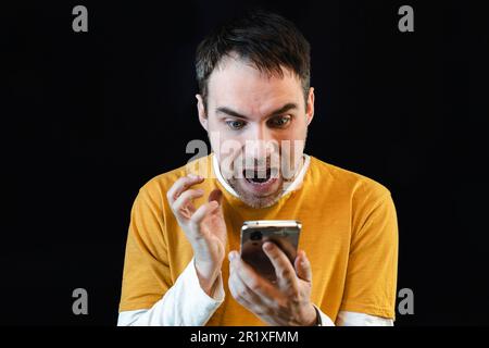 Surpris heureux homme tenant smartphone . un gars épaté lit le message sur le téléphone. Banque D'Images