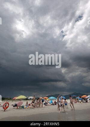 Des pluies torrentielles de nuages noirs sur la plage de Porto Giunco près de Villasimius, Sardaigne, Italie. Personnes en vacances en Italie. Mauvais temps et pluie Banque D'Images