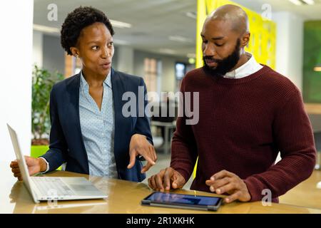 Des collègues afro-américains analysent les rapports de vente sur tablette numérique et ordinateur portable au bureau Banque D'Images