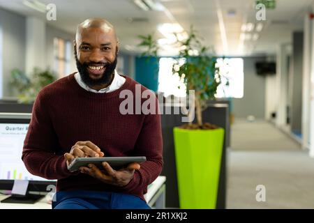 Portrait d'un homme d'affaires américain africain barbu travaillant sur une tablette numérique tout en étant assis sur un bureau Banque D'Images