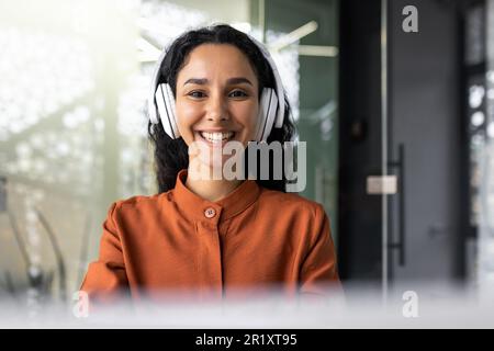 Portrait d'une femme indienne programmeur, femme dans un casque à l'écoute de musique, podcast audio, sourire et regarder la caméra, ingénieur développeur fermer à l'intérieur du bureau sur le lieu de travail, logiciel de codage. Banque D'Images