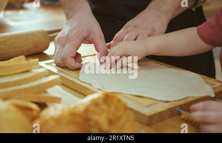 Bonne famille jeune appréciant faire de la pâte à tarte ou des pâtisseries dans la cuisine moderne ensemble, très heureux parents enseignant le petit fils comment faire cuire la boulangerie à la maison Banque D'Images