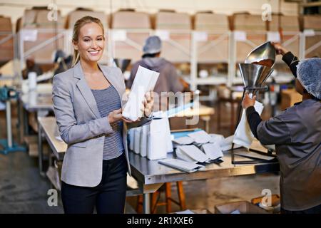 Bientôt pour être la tasse de café parfaite. Portrait d'un gestionnaire dans un entrepôt avec des travailleurs en arrière-plan. Banque D'Images