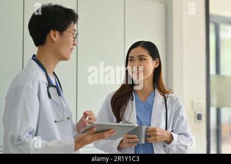 Deux médecins professionnels discutent des données de diagnostic des patients sur une tablette numérique, debout dans un bureau médical Banque D'Images