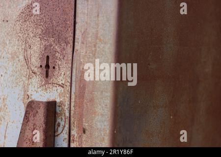 un trou de serrure sur un vieux coffre rouillé debout dans la rue près d'un mur de briques blanches sur l'asphalte à côté d'une boîte en aluminium perforée et de l'herbe verte Banque D'Images