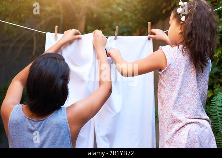 Travail d'équipe, linge suspendu et une mère et un enfant faisant des travaux ménagers, des corvées et occupé avec des vêtements. Nettoyage, la famille et le dos d'une petite fille aidant maman Banque D'Images