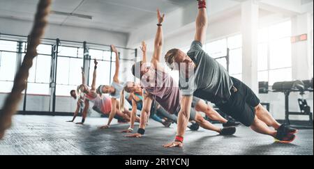 Cours de remise en forme, groupe et personnes faisant une séance de mise en forme dans la salle de gym pour la santé, le bien-être et la flexibilité. Sports, entraînement et athlètes faisant une planche latérale Banque D'Images