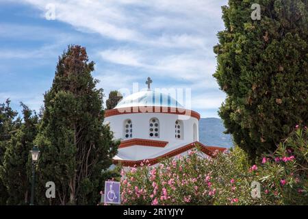 Île d'Andros, ville de Chora, Cyclades destination Grèce. Église orthodoxe blanche croix voûtée fenêtre dôme bleu, vue à travers l'arbre, ciel arrière-plan. Banque D'Images