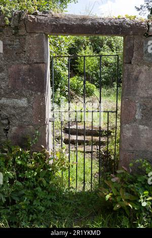 Ancienne porte de jardin à travers le mur de pierre, surexploitation et effritement. Banque D'Images