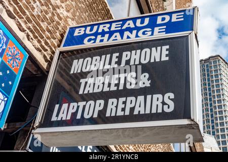 Un panneau sur un mur dans une rue de Londres annonçant le Bureau de change et les services de réparation de téléphone mobile, tablette et ordinateur portable Banque D'Images