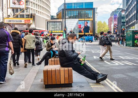 Les gens s'assoient sur des tabourets de bois sur le trottoir le long de Tottenham court Road à Londres pendant les heures de pointe. Banque D'Images