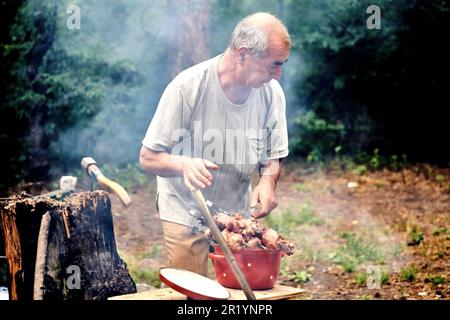 Vieux gai pensionné prépare la viande pour le barbecue pour la cuisson sur le feu de grill Banque D'Images