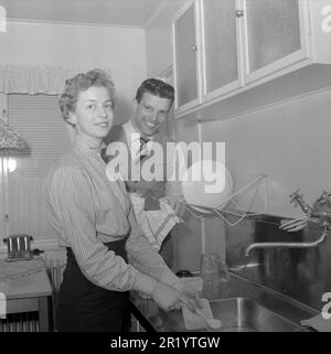 Dans la cuisine 1950s. Un jeune couple fait les plats dans la cuisine, elle nettoie les assiettes et il les sèche avec une serviette. Il est chanteur Cacka Israelsson, 1929-2013. Suède 1954. Conard réf. 2643 Banque D'Images