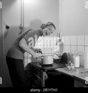 Dans la cuisine 1950s. Intérieur d'une cuisine et une jeune femme debout à la cuisinière de cuisine faisant un visage drôle tout en cuisinant quelque chose dans une casserole. Elle est actrice Maj-Britt Thörn, 1923-2023. Suède 1951 Conard réf. 1652 Banque D'Images