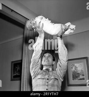 Homme du 1950s. Le danseur suédois Mario Mengarelli lors d'une séance photo à domicile avec son nouveau-né qu'il tient dans les mains au-dessus de sa tête. Suède 1952 réf. 1958 Banque D'Images