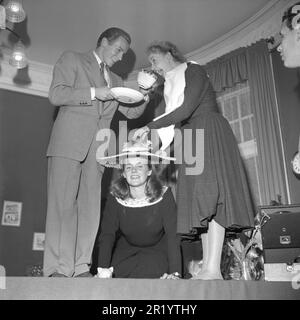 Amusez-vous dans le 1940s. Un homme et une femme avec une grande tasse de thé au-dessus d'une femme sur ses genoux, agissant comme une table avec des fruits sur son chapeau. Une image étrange sans explication autre que les filles font partie du groupe de danse et de spectacle Casselflickorna. Suède mars 1948. Conard réf. 917 Banque D'Images