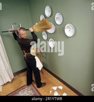 Jour de nettoyage en 1970s. Intérieur d'un homme qui nettoie le sol. Dans sa stupidité, il essaie de nettoyer les plaques accrochées au mur et, bien sûr, l'une d'entre elles tombe au sol et se brise en morceaux. Il est acteur Stig Grybe 1928-2017. 4 octobre 1972. Kristoffersson Banque D'Images