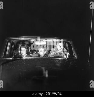 Conduite dans le 1950s. Un jeune homme sur le siège de conduite avec deux jeunes femmes à côté de lui sur le siège avant. Il se concentre sur la conduite dans la nuit sombre et ses yeux sont sur la route comme c'est une nuit de pluie. Suède 1959. Réf. BV99-12 Banque D'Images