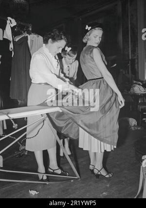 La mode des femmes en 1950s. La jeune mannequin est toujours debout pendant qu'un assistant reporte sa robe juste quelques instants avant que le modèle ne passe sur scène pour la montrer. C'est dans les détails bien sûr et une photo de l'arrière-plan. Suède 1951 Banque D'Images