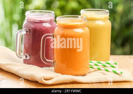 Différents délicieux smoothies dans des pots de maçon sur une table en bois sur fond flou Banque D'Images