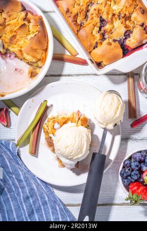 Tarte parée à la framboise aux baies, gâteau maison à l'éponge avec rhubarbe sucrée et fraise, servi avec boule de glace à la vanille, sur un k en bois blanc ensoleillé Banque D'Images