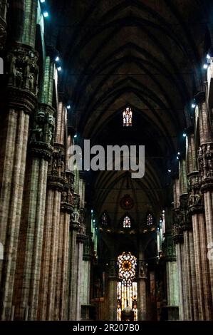 Colonnes massives en grappes, statuettes sculptées sur des capitols et lumière rouge dans la cathédrale de Milan, en Italie. Banque D'Images