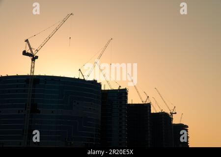 Silhouette de plusieurs grues à tour sur un site de construction moderne de gratte-ciel dans une scène de développement urbain au coucher du soleil, dans la ville de Dubaï, United Ara Banque D'Images