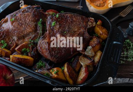 Plat à viande pour Thanksgiving avec queues de dinde rôties. Servi avec de la pumkine au noyer cendré, des pommes rouges, des oignons dans une rôtissoire sur une table rustique en bois Banque D'Images