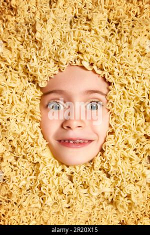 Image drôle avec le visage mignon de la belle petite fille, enfant peeking dehors Noodles arrière-plan. Amusement, nourriture, nutrition, fantaisie Banque D'Images