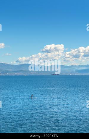 Personne méconnaissable paddle-board debout sur la mer Adriatique du golfe de Kvarner vue de la côte de la ville de Lovran, attention sélective Banque D'Images