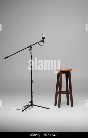 Chaise en bois marron debout près du microphone noir sur support en métal sur fond gris avec espace de copie, tabouret élevé en studio, image de stock Banque D'Images