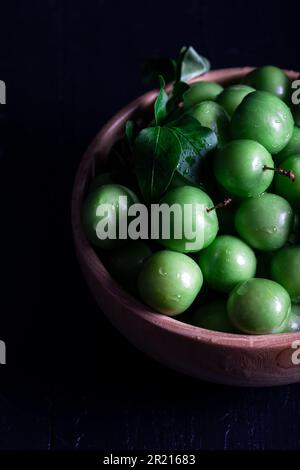 Prunes vertes fraîches dans un bol sur fond de bois. Gros plan. Banque D'Images