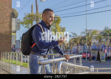 Jeune latino avec sac à dos regardant son téléphone mobile. Banque D'Images
